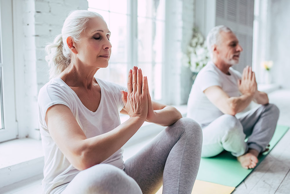 Ocean-Hills-Blog-Senior-Man-and-Woman-Exercising-Doing-Yoga-Sitting-Down-Indoors