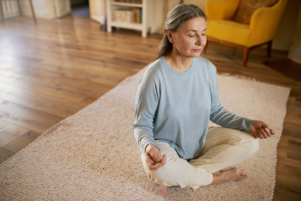 Senior woman sitting on floor meditating in living room