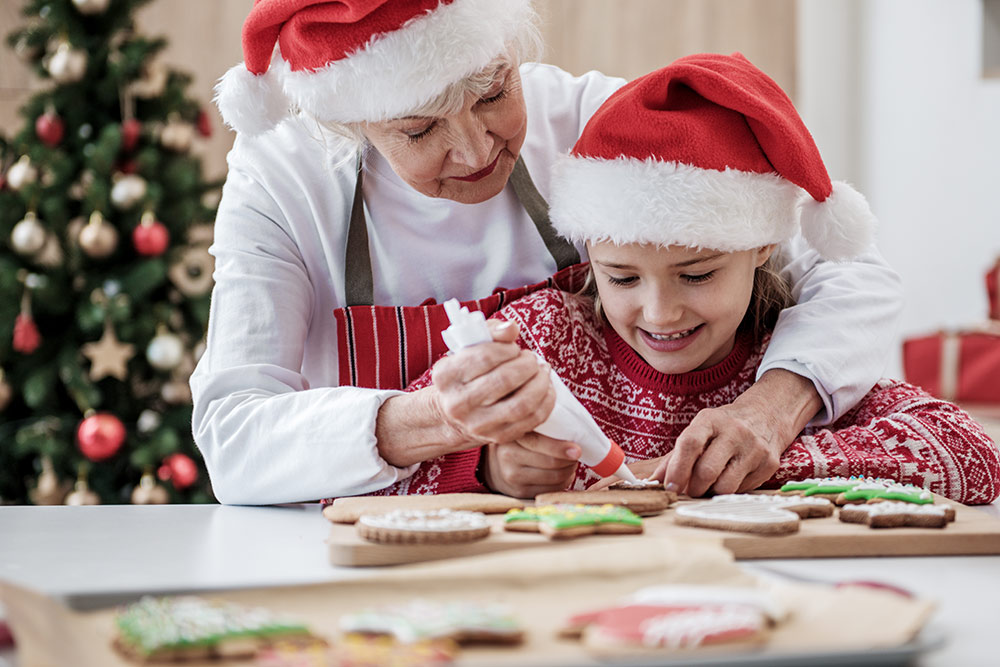 Senior woman and granddaughter decorating Christmas cookies in kitchen