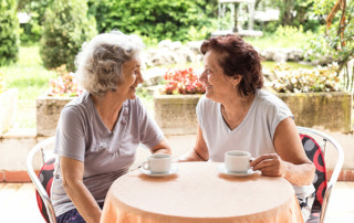 Happy senior women having coffee or tea sitting outside on patio at senior living community