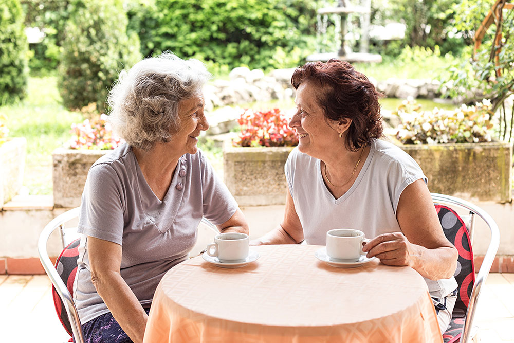 Happy senior women having coffee or tea sitting outside on patio at senior living community