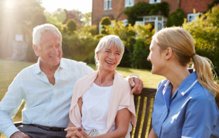 Happy senior couple sitting on bench with caregiver at assisted living home in Oceanside, CA