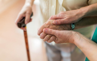 Caregiver holding senior hands, senior also holding walking stick in other hand