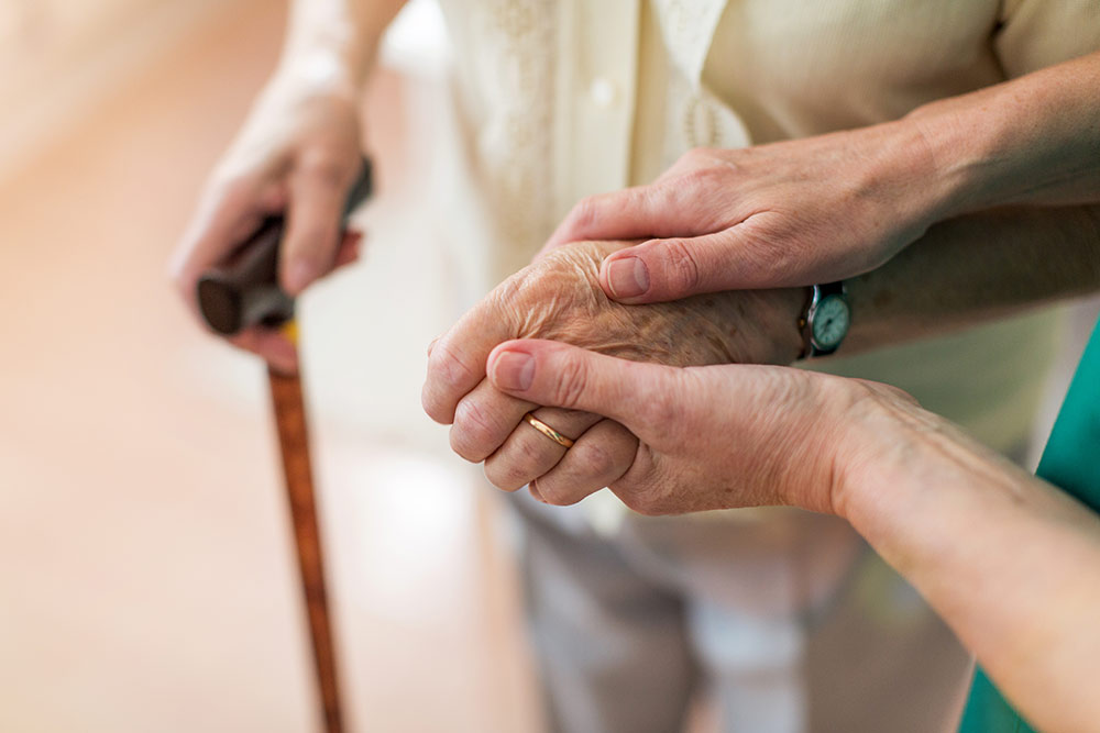 Caregiver holding senior hands, senior also holding walking stick in other hand
