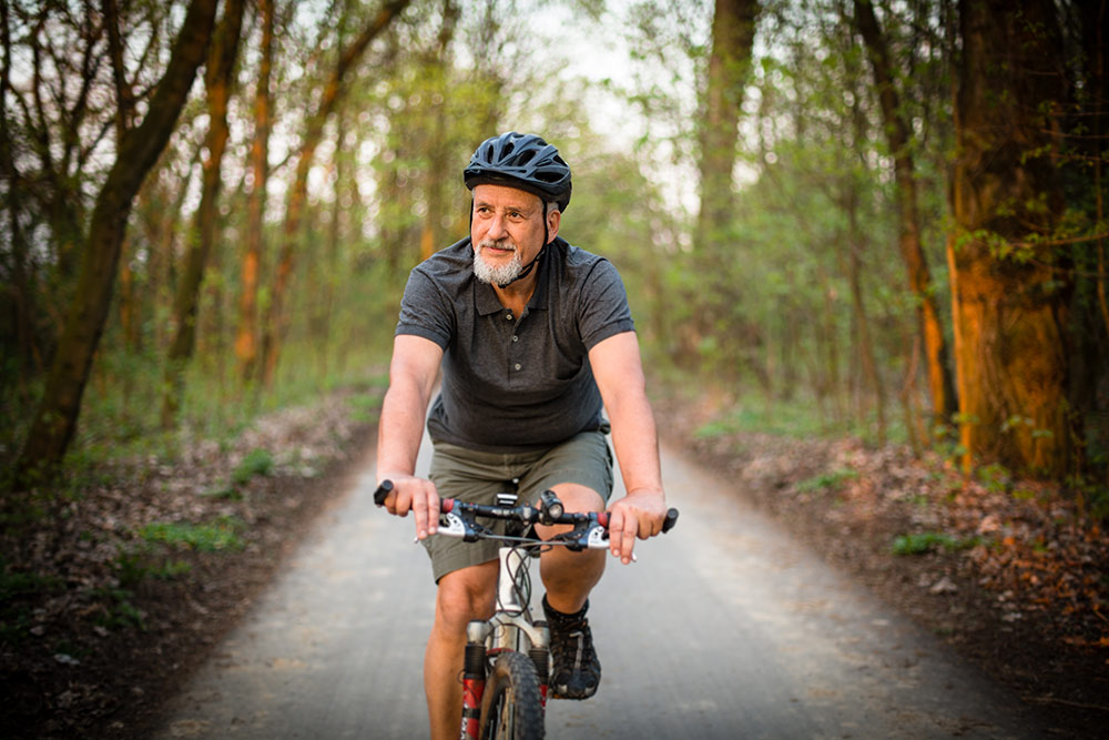 Senior man riding bike outside on road in wooded area